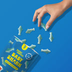Sweet Switch Baby Shark candy package on a blue background with shark candy laying shattered over the place and a hand reaching out to grab one sugar free