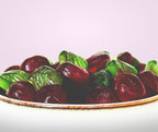 Gummy candies resembling cherries with green leaves on a white plate against a light purple background sugar free