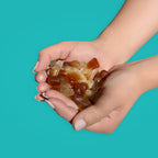 Hands holding a small pile of Cola Zero Candy against a teal background sugar free