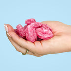 Hand holding pink gummy lips against a light blue background sugar free