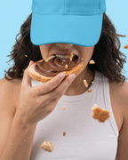 Person eating a chocolate-covered donut with a blue cap on a light blue background sugar free