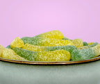 Green and yellow gummy worms on a white plate with a pink background sugar free