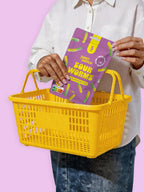 Person holding a purple package labeled 'Sour Worms' over a yellow basket against a pink background sugar free