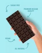 Hand holding a chocolate bar with text indicating sugar-free, premium Belgian quality, vegan, and all natural on a light blue background.