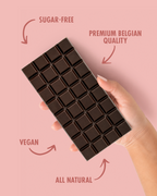 Chocolate bar held by a hand with text indicating sugar-free, premium Belgian quality, vegan, and all natural on a pink background. sugar free
