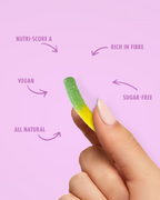 Hand holding a green and yellow gummy worm with nutritional information text on a pink background sugar free
