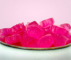 Pink gummy unicorns on a white plate with a light pink background sugar free